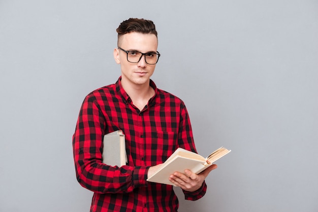 Joven serio en gafas y camisa sosteniendo el libro en las manos