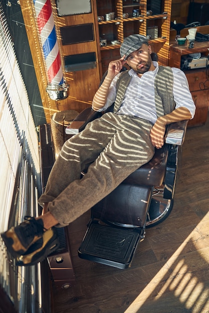 Un joven serio que parece moderno mientras está sentado en un sillón de barbero