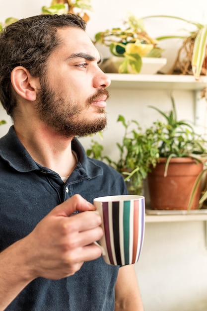 Un joven serio con una taza de café parado en el balcón