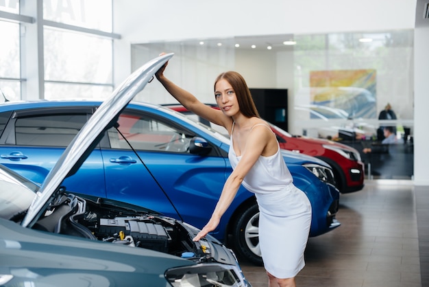 Una joven sexy inspecciona el motor del automóvil antes de comprar. Comprar un auto nuevo en un concesionario de autos.