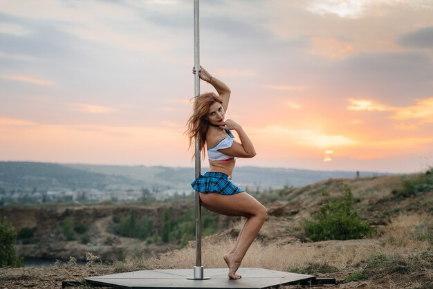 Una joven sexy realiza ejercicios increíbles en un poste durante una hermosa puesta de sol. Baile. Sexualidad.