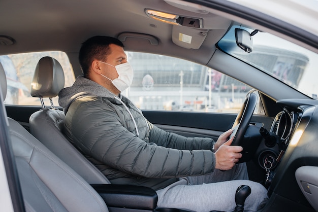 Un joven se sienta al volante con una máscara para su seguridad personal mientras conduce durante una pandemia y un coronavirus. Epidemia.