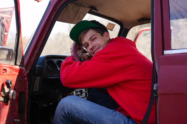 Foto joven se sienta en el asiento del conductor de un automóvil rojo, con la mano en el volante. conceptos vacaciones y viajes, vehículo