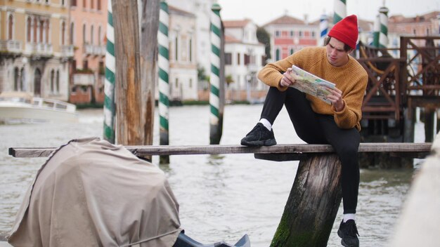 Un joven se sienta en el banco de la costa y mira el mapa en las calles de Venecia