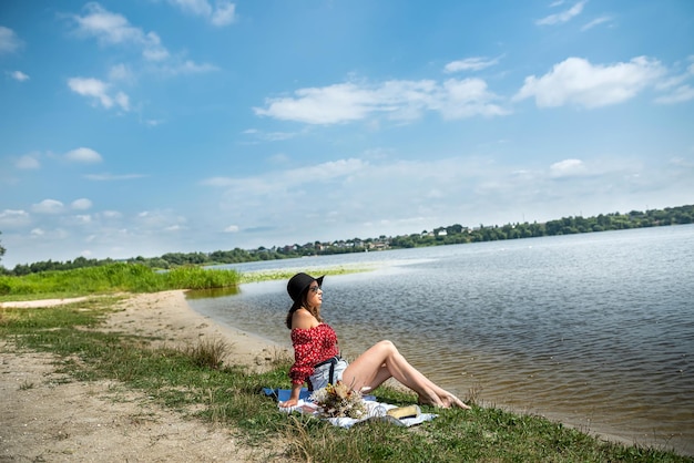 La joven se sienta cerca del estanque y el descanso disfruta de un caluroso día de verano en la naturaleza