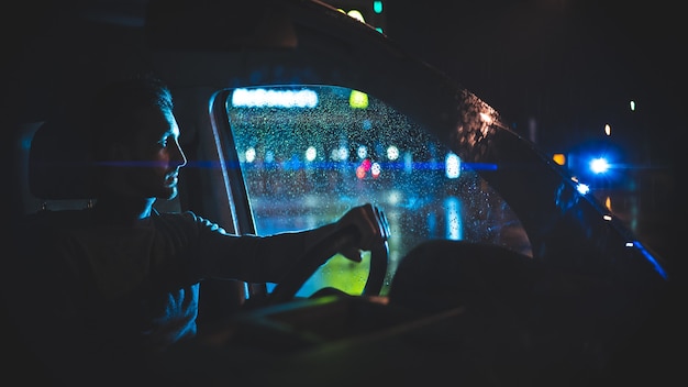 El joven se sienta en el coche en la calle lluviosa de noche