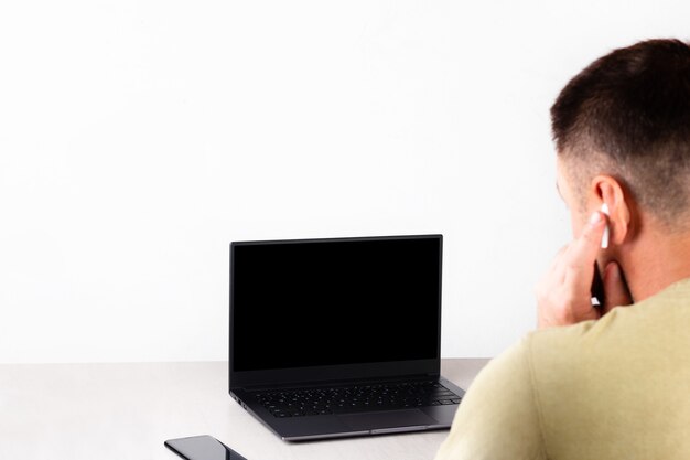 Un joven se sienta frente a una computadora portátil con una maqueta negra en la pantalla, el concepto de aprendizaje a distancia, transmisión en vivo, comunicación en línea