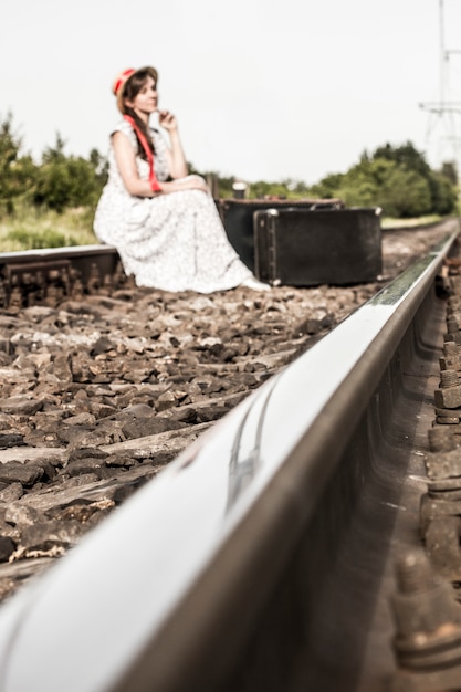 Una joven se sienta con una maleta en las vías del tren.