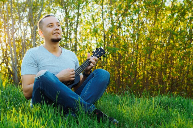 Joven se sienta tocando el ukelele en el parque.