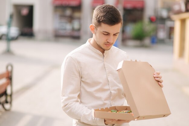 Foto joven siente hambre al abrir la caja de pizza al aire libre