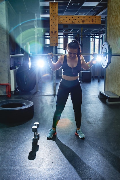 Foto una joven sincera y fuerte está entrenando con una barra en el gimnasio haciendo sentadillas y peso muerto real wokout