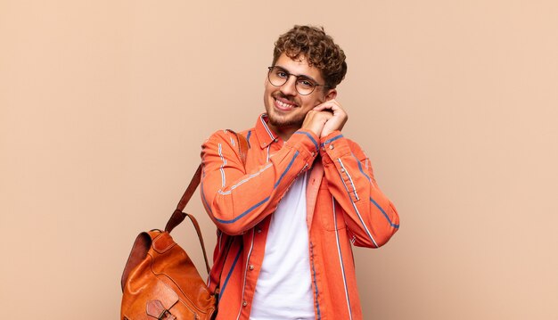 Joven sintiéndose enamorado y luciendo lindo, adorable y feliz, sonriendo románticamente con las manos al lado de la cara. concepto de estudiante