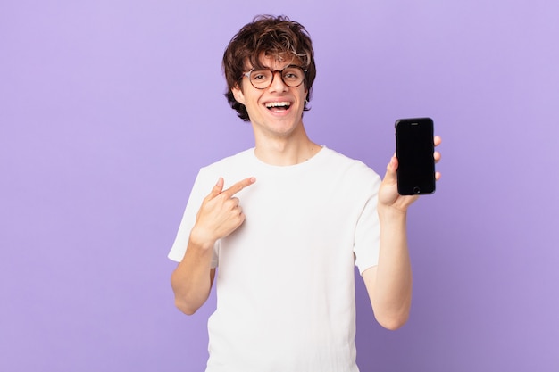 Joven sintiéndose feliz y apuntando a sí mismo con un emocionado y sosteniendo una celda