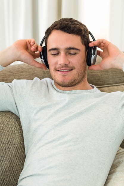 Joven sintiéndose relajado mientras escucha música con auriculares en la sala de estar