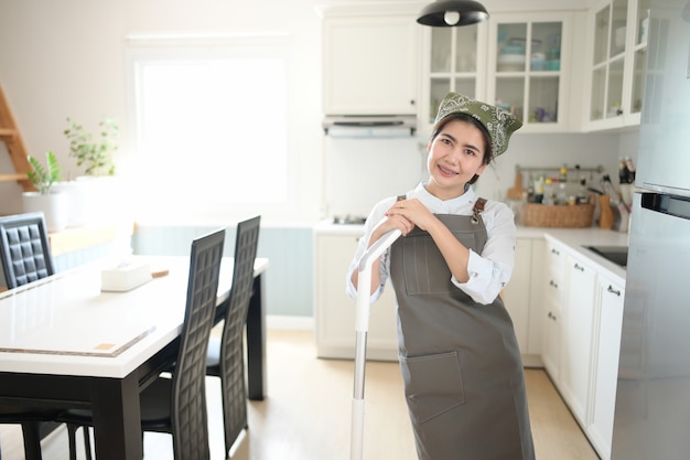 Una joven sirvienta limpiando la casa con un trapeador Hay una cocina como telón de fondo