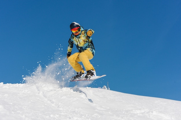 Joven snowboarder activo en ropa deportiva brillante saltando en la ladera de una montaña