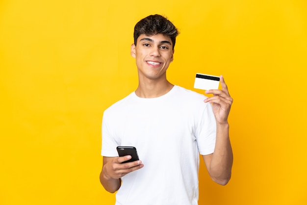 Joven sobre amarillo comprando con el móvil con tarjeta de crédito