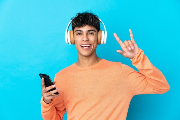 Joven sobre azul escuchando música con un móvil haciendo gesto de rock