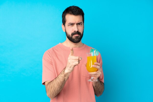 Joven sobre la celebración de un cóctel sobre la pared azul aislado frustrado y apuntando hacia el frente