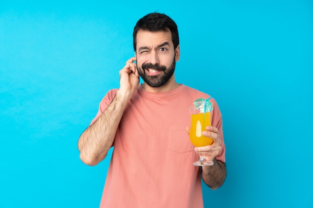 Joven sobre la celebración de un cóctel sobre pared azul aislado frustrado y cubriendo las orejas