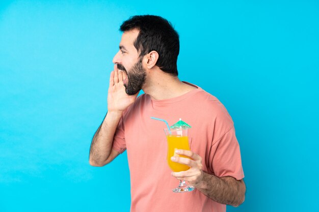 Joven sobre la celebración de un cóctel sobre pared azul aislado gritando con la boca abierta al lateral