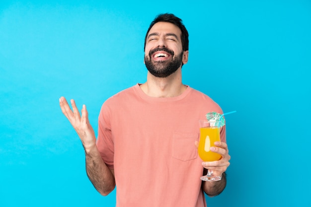 Joven sobre la celebración de un cóctel sobre la pared azul aislado sonriendo mucho