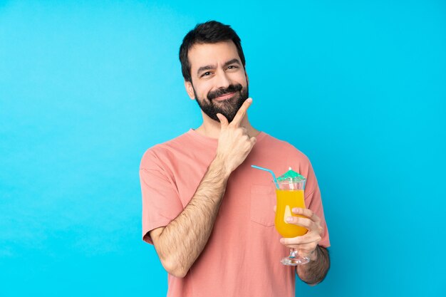 Joven sobre la celebración de un cóctel sobre pared azul aislado sonriendo