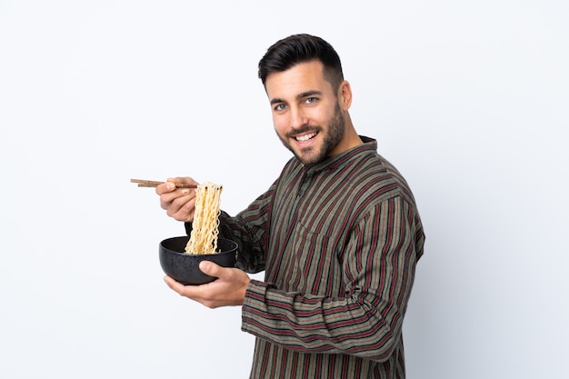 Joven sobre pared aislada sosteniendo un tazón de fideos con palillos