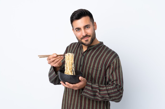 Joven sobre pared aislada sosteniendo un tazón de fideos con palillos