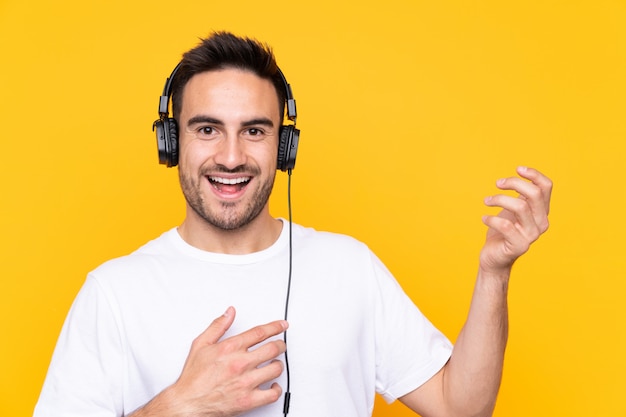 Joven sobre pared amarilla escuchando música y haciendo gesto de guitarra