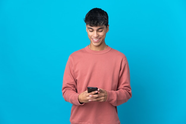 Foto joven sobre pared azul aislada enviando un mensaje con el móvil