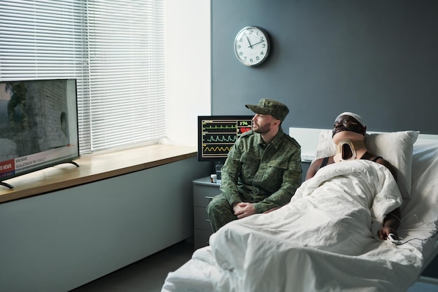 Joven soldado con uniforme militar sentado junto a la cama de un amigo herido