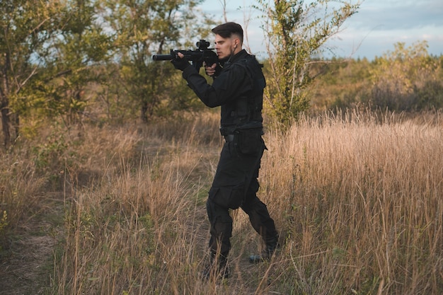 Joven soldado en uniforme negro apuntando con un rifle de asalto