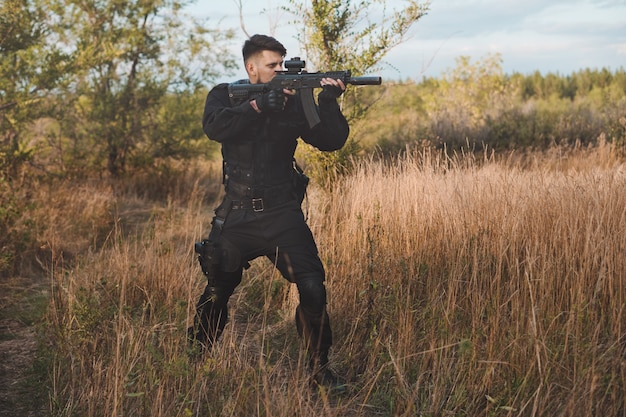 Joven soldado en uniforme negro apuntando con un rifle de asalto