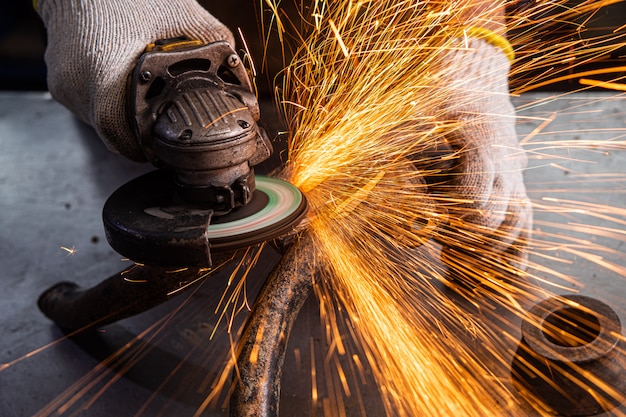 Un joven soldador en una amoladora de guantes azules de metal una amoladora angular en el taller, las chispas vuelan hacia un lado