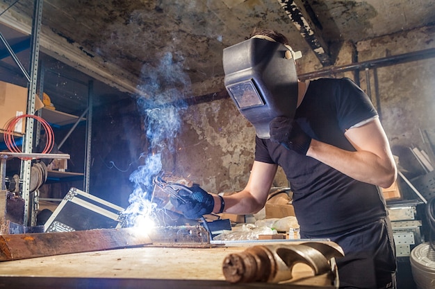 Un joven soldador masculino fuerte elaborando una máquina de soldadura de metales