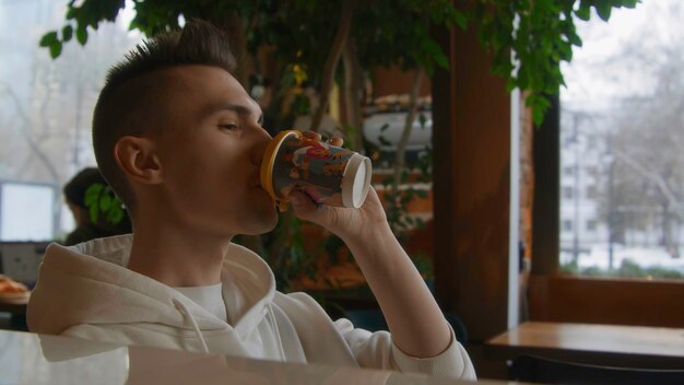 Un joven solo bebe café en una cafetería. Imágenes de archivo. Un joven guapo está bebiendo café solo.