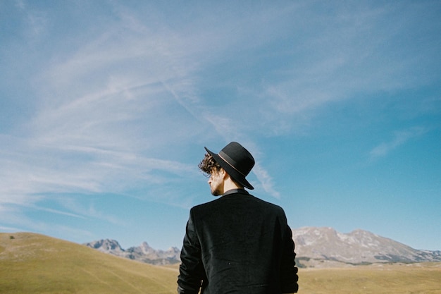 Joven en un sombrero contra el telón de fondo de las montañas y el retrato de vista trasera del cielo