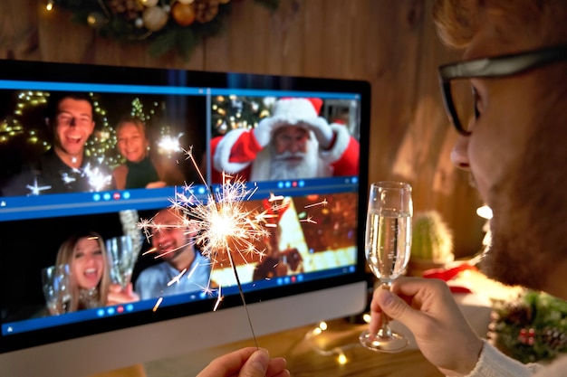 Foto joven con sombrero de navidad bebiendo champán sosteniendo una chispa hablando con amigos en una llamada de video virtual celebrando una fiesta de año nuevo feliz a distancia chat en línea en casa por encima del hombro vista de la pantalla