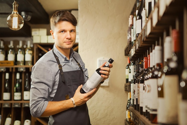 Joven sommelier sosteniendo una botella de vino tinto en bodega