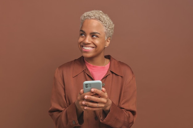 Joven soñadora mujer afroamericana con teléfono móvil sonriendo y mirando hacia otro lado