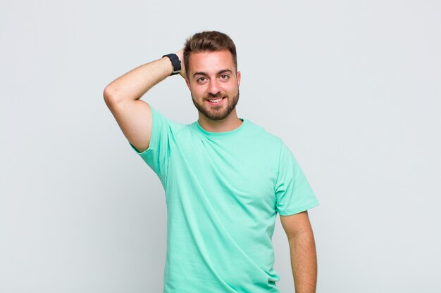 Joven sonriendo alegre y casualmente, tomando la cabeza con una mirada positiva, feliz y segura