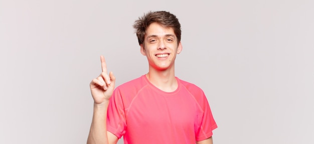 Joven sonriendo alegre y felizmente, apuntando hacia arriba con una mano para copiar el espacio