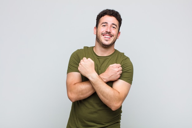 Joven sonriendo alegremente y celebrando, con los puños cerrados y los brazos cruzados, sintiéndose feliz y positivo