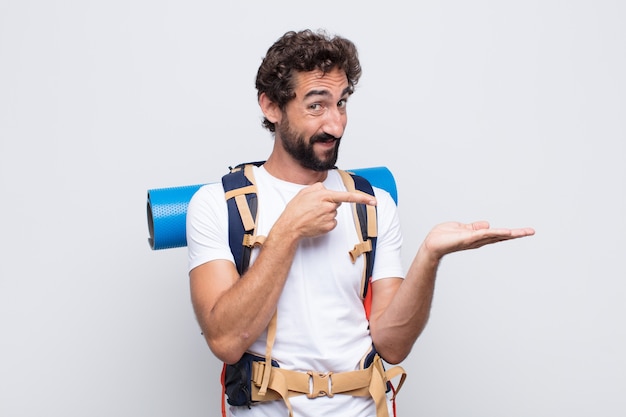 Joven sonriendo alegremente y señalando para copiar el espacio en la palma del costado, mostrando o publicitando un objeto