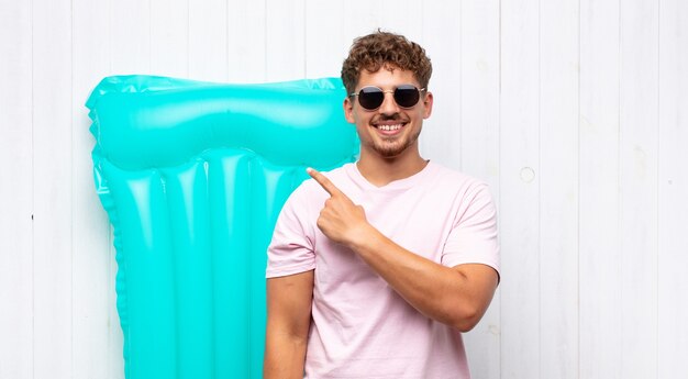 Joven sonriendo alegremente, sintiéndose feliz y apuntando hacia un lado y hacia arriba