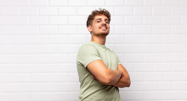 Joven sonriendo alegremente, sintiéndose feliz, satisfecho y relajado, con los brazos cruzados y mirando hacia un lado