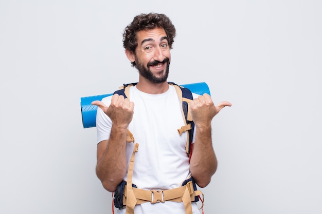 Joven sonriendo con alegría y luciendo feliz, sintiéndose despreocupado y positivo con ambos pulgares hacia arriba