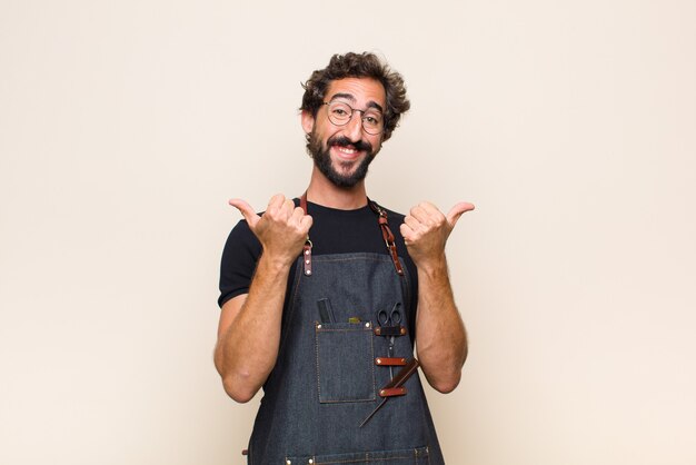 Joven sonriendo con alegría y luciendo feliz, sintiéndose despreocupado y positivo con ambos pulgares hacia arriba