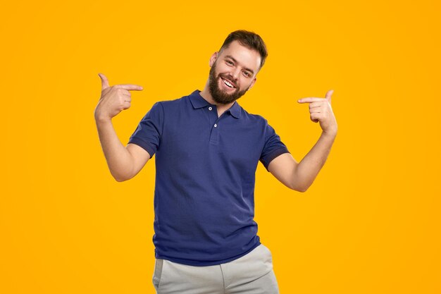 Joven sonriendo a la cámara y apuntándose a sí mismo en el estudio